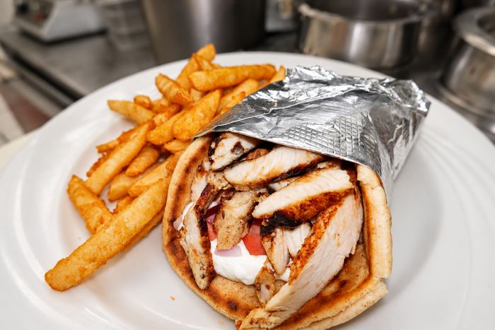 Chicken gyro pita with tomato, onion and sauce, wrapped in foil, with a side of fries