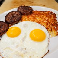 Two sunny-side-up eggs with sausage patties and crispy homemade hash browns